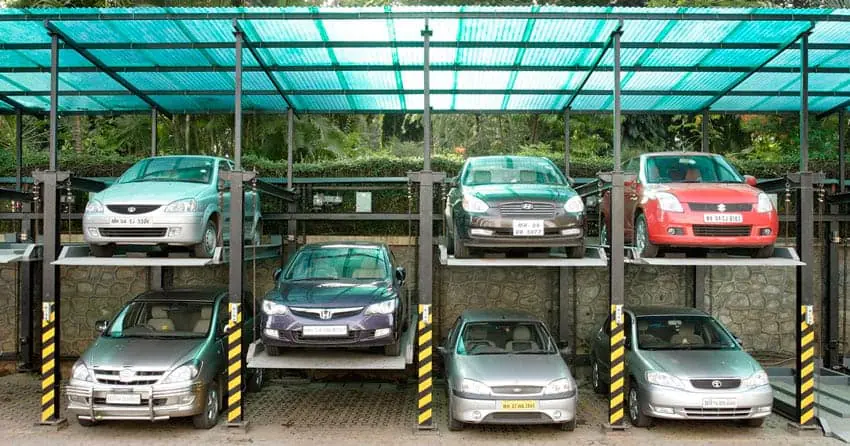 Two tier outdoor car stacker under a green polycarbonate canopy holding four cars on the upper deck and three parked below.