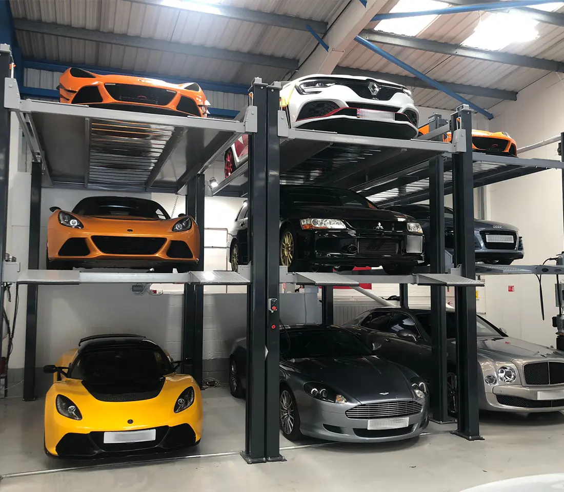 Silver Range Rover Velar parked on the upper platform of a two post lift above a black SUV in an indoor garage bay.