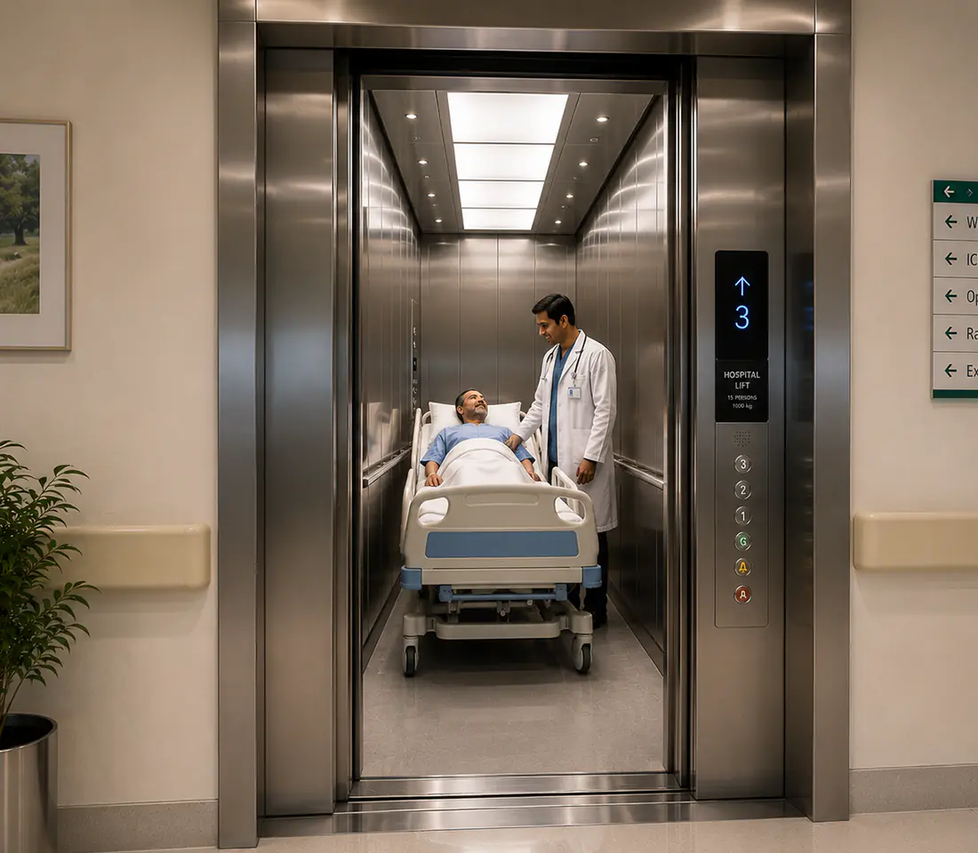 Empty stretcher lift cabin with white panelled walls, dual handrails, and stainless steel doors open onto a hospital corridor.